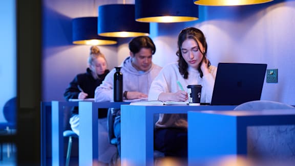 Three people are working at a table with laptops.