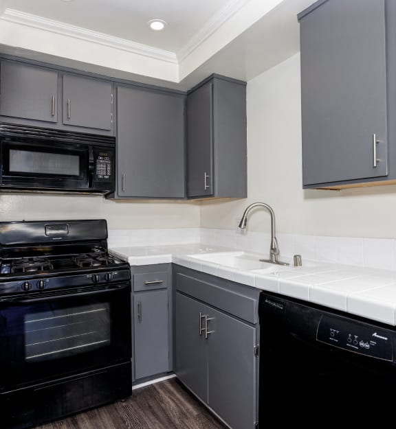 a kitchen with black appliances and white counter tops and gray cabinets