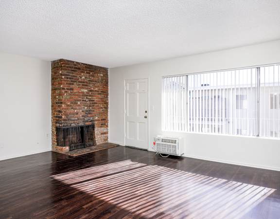 an empty living room with a brick fireplace and hard wood floors