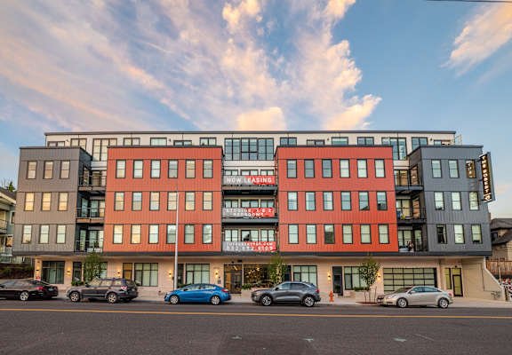 A multi-story building with a red and black facade is surrounded by parked cars.