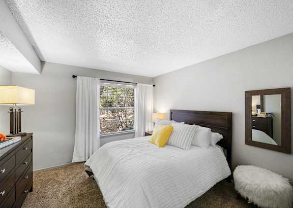 A bedroom with a large bed and a window with white curtains.