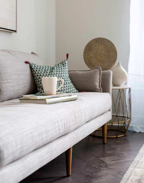 A white couch with a green pillow and a book on it. at The Pennsylvanian Apartments, Pittsburgh, Pennsylvania