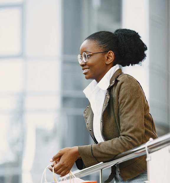 A woman with a white shirt underneath a brown jacket is holding shopping bags.