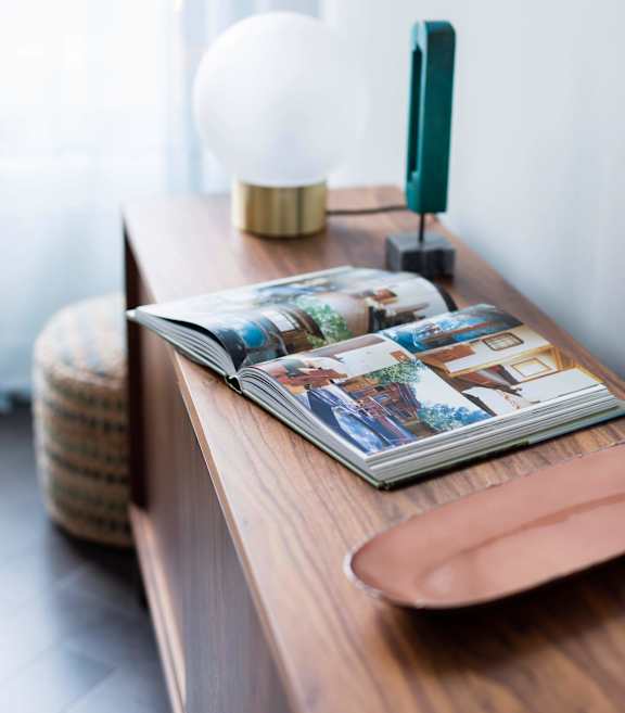 A magazine is open on a wooden table with a lamp and a green object beside it at The Pennsylvanian Apartments, Pittsburgh, Pennsylvania