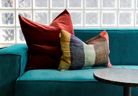 a blue couch with pillows in front of a glass wall