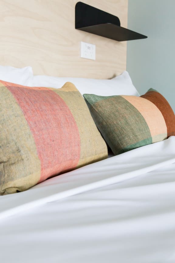 two multicolored pillows on a bed with white sheets