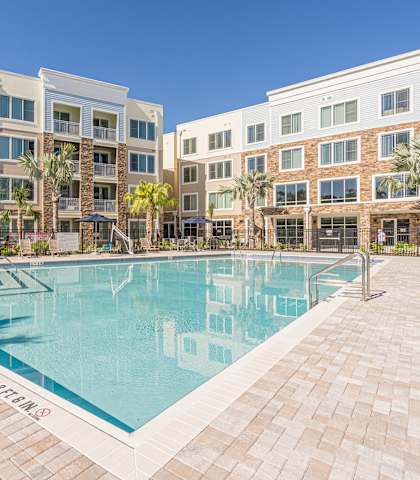 A pool surrounded by a brick patio and palm trees. at Sandpiper Glen 62+ Apartments, Orlando, FL