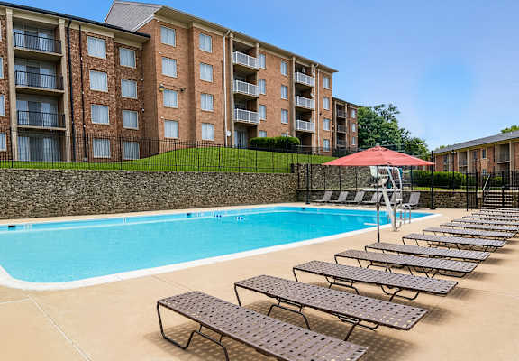A swimming pool with sun loungers and a red umbrella in front of a brick building.