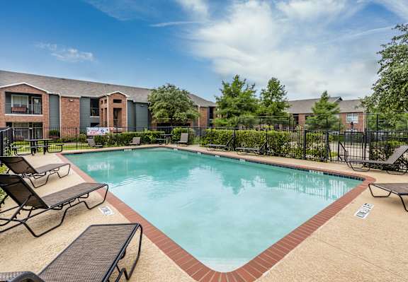 A swimming pool surrounded by lounge chairs and a fence.