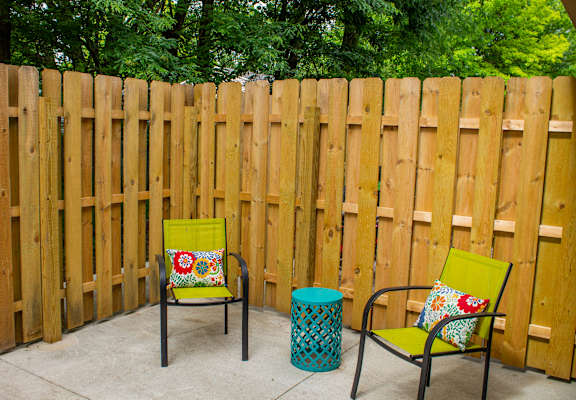 A yellow chair with a floral pillow sits in front of a wooden fence.
