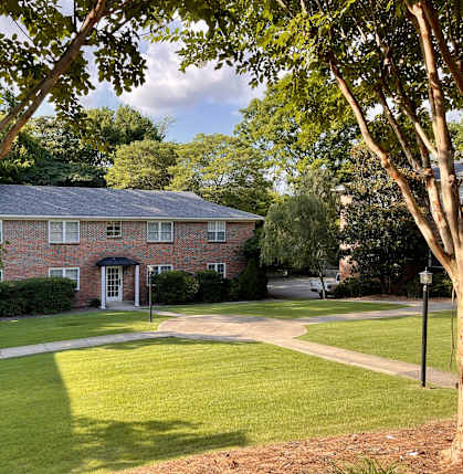 the front of a brick house with a lawn and trees