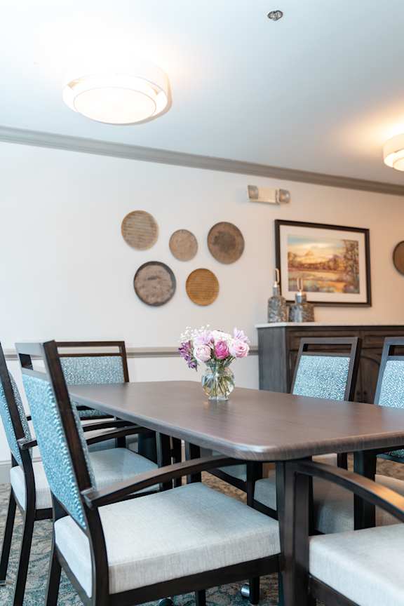 A dining table with chairs and a vase of flowers on it.