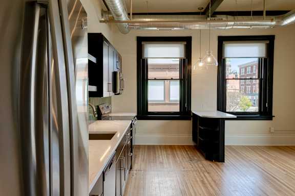 A kitchen with a refrigerator on the left and a table with a black cabinet on the right.
