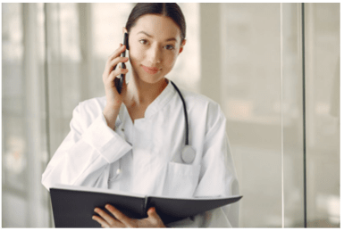 A woman in a white coat holding a clipboard and talking on a phone.