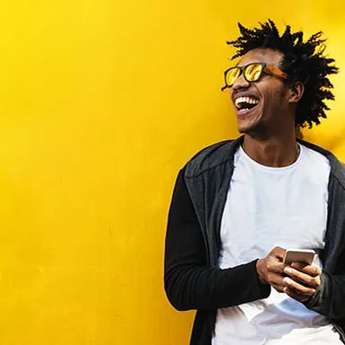 a man wearing glasses laughing while holding a cell phone