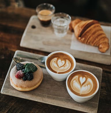 Lattes and baked goods on a wood tray.