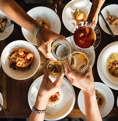 A group of friends cheering beer and wine over an italian dinner.