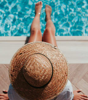 A woman with a straw sunhat sitting next to a pool