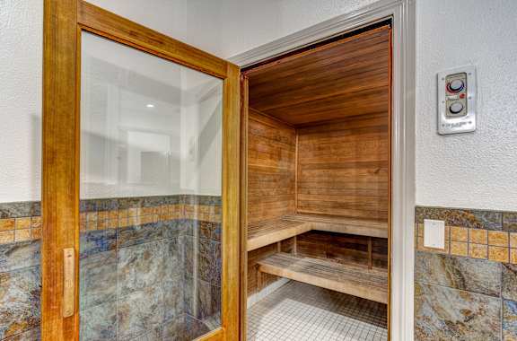 A wooden door with a glass window is open to a bathroom with a bench.