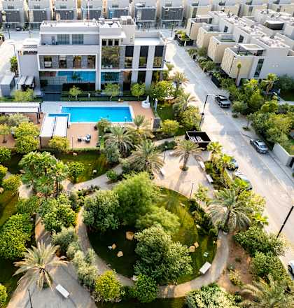 A large white building with a pool in the middle of a green area surrounded by trees.