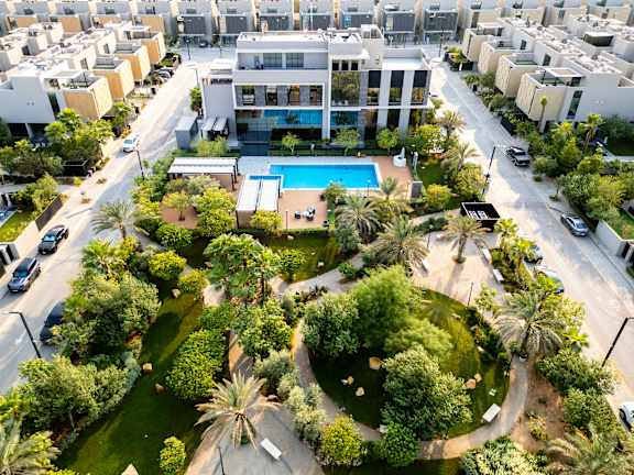 A large white building with a pool in the middle of a green area surrounded by trees.