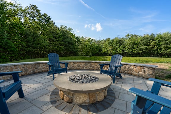 A fire pit surrounded by blue chairs and a stone wall.