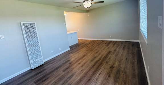 an empty living room with wood flooring and a ceiling fan