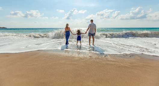 A family of three is standing on the beach with the ocean in the background.
