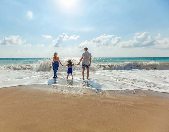 A family of three is standing on the beach with the ocean in the background.