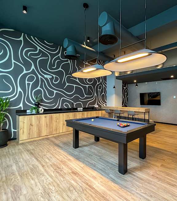 A pool table is in the middle of a room with a wooden floor and a wall with a black and white pattern.