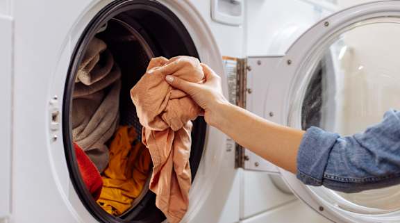 A person is holding a pair of dirty laundry in front of a washing machine.