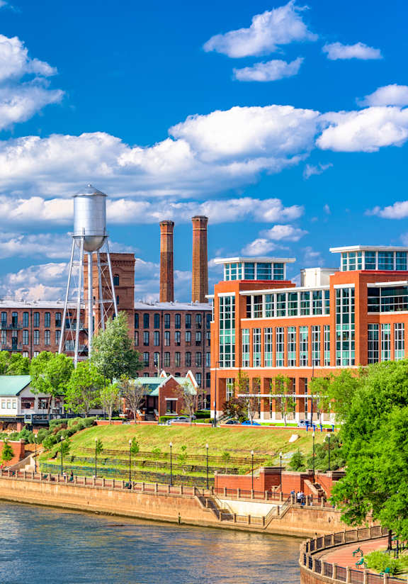 A cityscape with a river in the foreground and a mix of modern and older buildings.