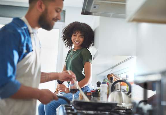 A man and a woman are standing in a kitchen, with the woman holding a glass of red wine.