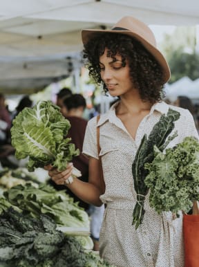 a woman holding a bunch of cabbages at a farmers market