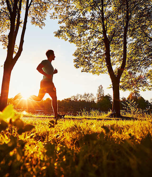A person running in a field with trees and the sun setting in the background.