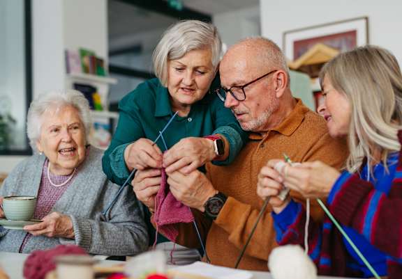 A group of people are gathered around a table knitting.