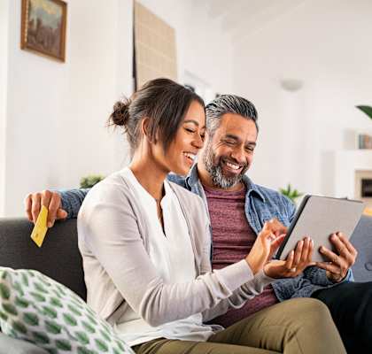 a couple sitting on a couch looking at a tablet computer