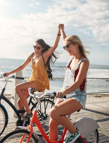 two women riding bikes along the beach