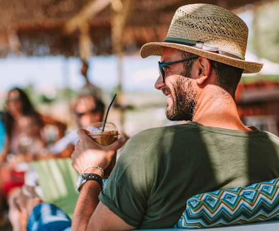 a man in a hat and sunglasses sits on a beach with a drink in his hand at Lakes at Suntree, Melbourne, Florida