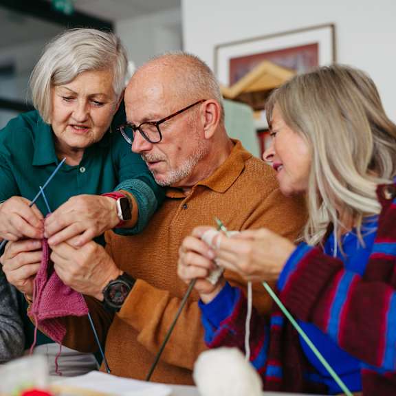 A group of people are gathered around a table knitting.