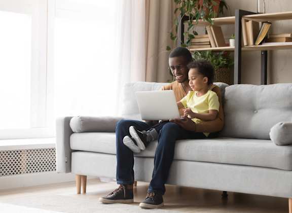 A man and a child are sitting on a grey couch.