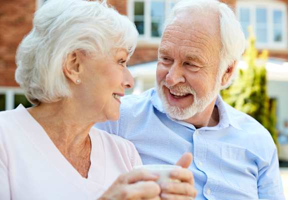 an elderly man and woman sitting on a bench and looking at each other