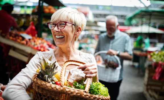 an older woman holding a basket of vegetables in a grocery store at The Rialto, Orlando, FL