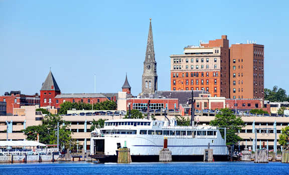 A cityscape with a church steeple and a large white boat docked in the water.