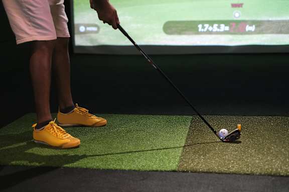 A man is playing golf in front of a screen that shows his score.