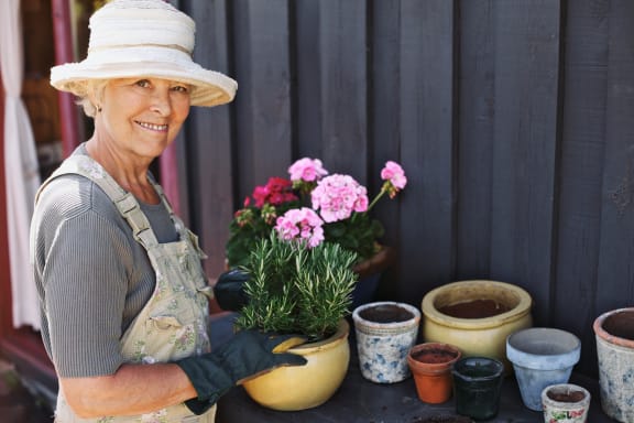 A woman in an apron standing next to pots of flowers and gardening.