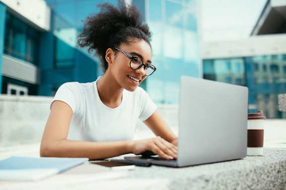 a woman sitting at a table using a laptop computer at Apex Mission Valley, San Diego, CA, 92108