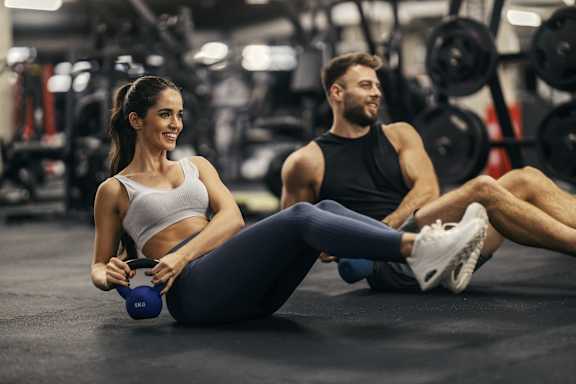 a man and a woman sitting on the gym floor with weights at Apex Mission Valley, San Diego, CA, 92108
