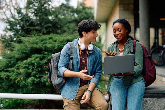 a man and a woman laughing while looking at a laptop computer
