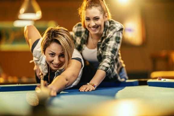 two women playing a game of pool on a blue pool table at Apex Mission Valley, San Diego, CA